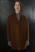 Load image into Gallery viewer, A person with short hair and red lipstick stands against a dark background, wearing a Bamford Double-face Cashmere | Tobacco. The gray sleeves of an inner garment peek out from the coat's sleeves. The person has a calm and composed expression.