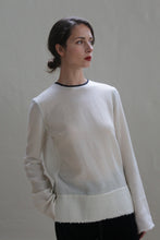 Load image into Gallery viewer, A woman with dark hair is styled in a low bun, looking off to the side with a soft, pensive expression. She is wearing a Crewneck shirt - Japanese Wool Gauze | Undyed with black accents on the cuffs. The background is a plain, neutral color, keeping the focus on her.