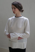 Load image into Gallery viewer, A person with long dark hair and red lipstick stands against a plain background. They are wearing a loose-fitting, long-sleeved **Crewneck shirt - Japanese Wool Gauze | Undyed** and dark pants. Their head is slightly tilted to the side, and their arms are crossed in a relaxed manner, embodying sustainable design.