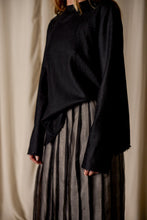 Load image into Gallery viewer, A person standing against a beige curtain background is wearing a Crewneck shirt - Japanese Wool Gauze | Black and a high-waisted, ankle-length, pleated skirt made from Japanese wool gauze with black and grey vertical stripes. The focus is on the sustainable design of the clothing, without showing the full face of the person.