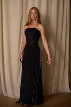 Load image into Gallery viewer, A woman with long blonde hair stands in front of beige curtains. She is wearing a Layered Skirt w/ Hand Pleats | Crepe de Chine with a custom houndstooth stripe and a fitted bodice. The skirt has a slit and is adorned with small silver embellishments along the edges. She has a neutral expression, and her arms are by her sides.
