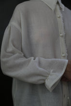 Load image into Gallery viewer, Close-up view of a person wearing a sheer white long-sleeved Poet Shirt - Japanese Wool Gauze | Undyed with pearly buttons. The fabric appears translucent, and the shirt has a loose, relaxed fit. Featuring sustainable design using Japanese Wool Gauze, the background is a solid dark color.