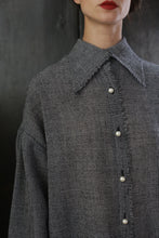 Load image into Gallery viewer, Close-up of a person wearing a Poet Shirt - Japanese Wool Gauze | BW Houndstooth, featuring pearl-like buttons. The background is dark, and the person's face is partially visible, showing red lipstick and a neutral expression, exuding a hint of Byronesque flair.