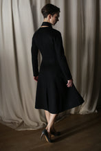 Load image into Gallery viewer, A person wearing The Ballerina Coat in Doubleface Cashmere Black and high heels stands on a wooden floor before light-colored curtains, partially turned away from the camera, highlighting a tailored silhouette that exudes luxury fashion.