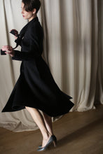 Load image into Gallery viewer, In front of beige curtains, a woman gracefully spins in "The Ballerina Coat | Doubleface Cashmere Black," exuding elegance with her short hair and stylish outfit. The blurred motion captures her fluid movement, while the wooden floor adds warmth to this luxurious fashion scene.