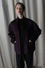 Load image into Gallery viewer, In front of a light-colored curtain backdrop, an individual wears the Bamford Short Double-Face Cashmere jacket in a rich aubergine shade, paired with black pants. With their hands in the jacket's pockets and sporting short dark hair, they exude a contemporary style with modern tailoring.
