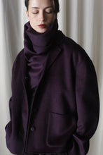 Load image into Gallery viewer, A person wears a dark purple oversized jacket with an X Scarf in aubergine, both crafted from double-faced cashmere. Standing against a white curtain backdrop, they have hands in pockets and gaze slightly downward.