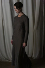 Load image into Gallery viewer, A woman with short hair stands in a dim room, wearing the Long Sleeved Crewneck Dress. Flowing drapes hang behind her as she gazes downward with a calm expression, highlighting the dress’s timeless handmade San Francisco elegance.
