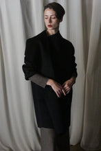 Load image into Gallery viewer, A person stands before draped white curtains, wearing the Winston Long Double-face coat in black over lighter clothing. They have short, styled hair and a poised expression, with hands gently clasped. The classic hues and dim lighting create a serene, contemplative mood.