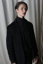 Load image into Gallery viewer, A person with short hair, dressed in the Unisex Blazer Double-Face Cashmere in charcoal, stands confidently against a backdrop of white curtains. The lighting casts a dramatic shadow, accentuating their poised expression.