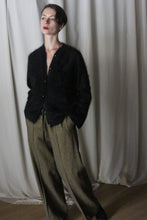 Load image into Gallery viewer, A person stands against a cream curtain, wearing a black fuzzy cardigan and high-waisted moss herringbone brushed cotton trousers. They have short hair, red lipstick, and pose with hands in pockets, gazing thoughtfully to the side, subtly nodding to Atelier Lan Jaenicke's elegant aesthetic.