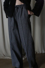 Load image into Gallery viewer, A person dons high-waisted, wide-legged gray pants made from brushed cotton twill with a black drawstring and a fuzzy black top. Their hands rest in the pockets against a light curtain backdrop, reminiscent of an Atelier Lan Jaenicke silhouette.