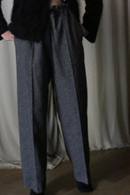 Load image into Gallery viewer, A person stands in Atelier Lan Jaenicke's Brushed Cotton Trousers in Blue Herringbone, hands casually tucked in pockets. The cotton twill pants complement their dark top, while a light curtain gracefully frames the wooden floor.