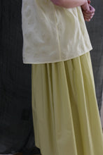 Load image into Gallery viewer, A person wears the Work Shirt in Textured Lawn Citrine with a matching flowing yellow skirt, standing in front of a dark fabric backdrop and clasping their hands behind their back.