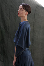 Load image into Gallery viewer, A woman with short brown hair wears the Kimono Top | Sandwashed Silk Charmeuse Teal, standing in profile against a muted green fabric backdrop and gazing upward with a calm expression.