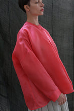 Load image into Gallery viewer, A person with short dark hair stands sideways, eyes closed, wearing an oversized bright pink Qipao Blouse | Silk Organza Sakura by Atelier Lan Jaenicke against a dark, textured fabric background.