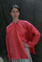 Load image into Gallery viewer, A woman poses with one hand on her hip, wearing the Qipao Blouse | Silk Organza Sakura in bright pink and a light skirt, set against a dark, textured background.