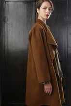 Load image into Gallery viewer, A woman with short, dark hair stands in front of a dark wooden backdrop, wearing a long, tobacco-colored coat. She is looking at the camera with a neutral expression and has red lipstick. The Winston Long Double-face coat features a relaxed construction with wide lapels.