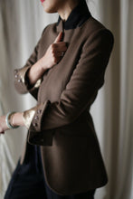 Load image into Gallery viewer, A person wearing the "Sloane" blazer, characterized by its brown hue, rolled-up sleeves, and structured shoulders, paired with a black shirt underneath, is holding the lapel of the blazer. The image is taken from the side, focusing on the upper body against a softly blurred, neutral backdrop.