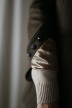 Load image into Gallery viewer, Close-up of a person's arm showing detailed fashion elements. The person is wearing the Sloane, a beige sweater underneath a dark brown coat with structured shoulders. The coat boasts turned-up sleeves revealing a shiny beige lining and three black buttons at the cuff.