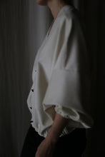 Load image into Gallery viewer, In dim lighting, a person showcases the Blanc de Chine: a loose-fitting white top with wide sleeves and black pants, highlighting its zero-waste design and commitment to sustainable fashion.