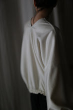 Load image into Gallery viewer, A person wearing a loose, light-colored Blanc de Chine blouse stands with their back to the camera against a softly lit background. The image is slightly out of focus, creating a serene atmosphere that highlights the elegance of zero-waste design.