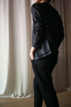 Load image into Gallery viewer, A person dressed in a black long-sleeve top and trousers stands in front of light-colored curtains, wearing the Waxed Linen Blazer with one hand in their pocket. The individual's face is not visible in the image.