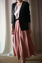 Load image into Gallery viewer, A person is standing indoors wearing a Waxed Linen Blazer over a white top paired with a flowing pink skirt. The image cuts off at the person's neck and is set against a softly lit, neutral background with light curtains.