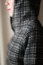 Load image into Gallery viewer, A person is shown in profile wearing the Alex Hoodie | Plaid, handmade in San Francisco. The focus is on the black and white checkered pattern of the hooded jacket, with a blurred background highlighting its unique craftsmanship.