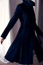 Load image into Gallery viewer, A person wearing the Hyde, a dark and elegant skirted trench with a high collar, spins gracefully. The long sleeves and flared hem are captured mid-movement against a softly lit backdrop.