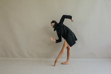 Load image into Gallery viewer, A dancer in a black Stamford Long cashmere coat poses gracefully on pointe shoes against a plain backdrop. One arm is elegantly bent forward while the other, accentuated by the coat's collar, extends behind, capturing a moment of fluid motion and balance.