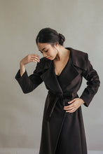 Load image into Gallery viewer, Wearing a luxurious Malvern double-breasted coat in dark brown, a person stands against a plain light background. Their hair is styled in a neat bun as they look down, one hand raised near their face and the other resting on their waist.