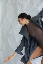 Load image into Gallery viewer, Wearing the Stamford Long, a person poses gracefully against a crumpled white paper backdrop, extending their arm and turning their head to the side with a serene expression. The high-collar of the dark gray coat complements their brown outfit beautifully.