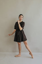 Load image into Gallery viewer, A woman gracefully poses in a brown Wexley A-line dress and ballet shoes, balancing on one leg with her arm raised against a plain background.