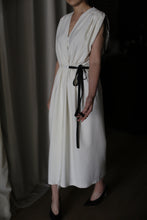 Load image into Gallery viewer, Person wearing a sleeveless, white raw silk Lune dress with a black ribbon tied at the waist. The background is dimly lit and appears to include curtains, and the person’s face is outside the frame. The person is also wearing black pointed-toe shoes.