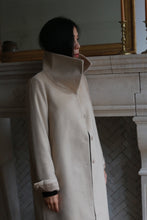 Load image into Gallery viewer, A person with long dark hair is standing in a Stamford Long cashmere coat with a high collar, looking to the side. They are positioned in front of a decorative stone fireplace with a large mirror above it.