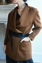 Load image into Gallery viewer, A person wearing a stylish brown coat, cinched at the waist with a Leather Obi with Grosgrain Ribbon. The coat, crafted from genuine lambskin, features large lapels and pockets. Beneath the coat, they have on a black dress and accessorize with a delicate gold necklace, while their hair is pulled back. Their face is partially visible as they look to the side.