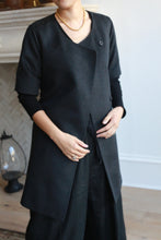 Load image into Gallery viewer, Clad in a dark gray Wexley double-breasted coat over a black shirt and pants, a short-haired individual stands indoors, their hands gently clasped near the middle. A glass lantern sits on the wooden floor in the background.