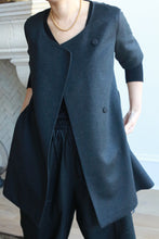 Load image into Gallery viewer, Wearing a stylish, dark gray Wexley woven cashmere coat featuring an asymmetrical buttoned front and short sleeves over a black outfit, accessorized with a gold necklace. Posing indoors with one hand in their pocket.