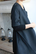 Load image into Gallery viewer, A person in a dark, long-sleeved Wexley double-breasted coat and a gold necklace stands near a fireplace adorned with decorative glass lanterns.