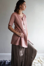 Load image into Gallery viewer, A person wearing the Wexley double-breasted coat over a pink top, paired with wide-legged brown pants, stands indoors. They have shoulder-length brown hair and face sideways, gazing out of view against a light gray wall with a white-framed baseboard.