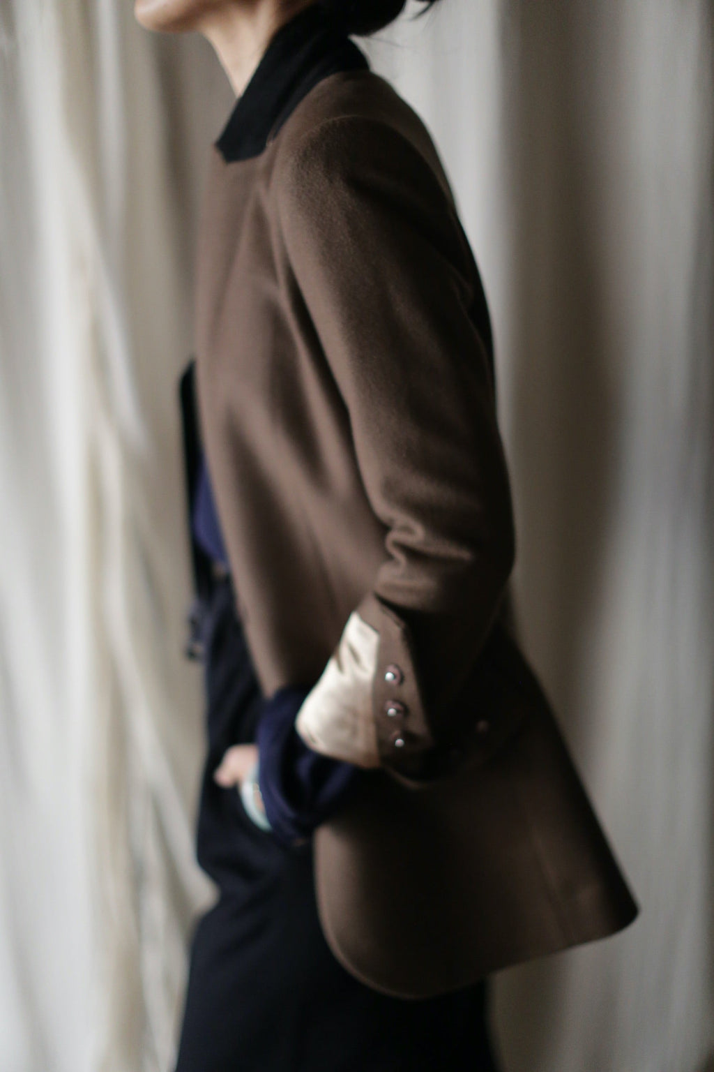 A person wearing a Sloane | Taupe / Black equestrian length cashmere blazer with a folded cuff over a black collared shirt and black trousers.