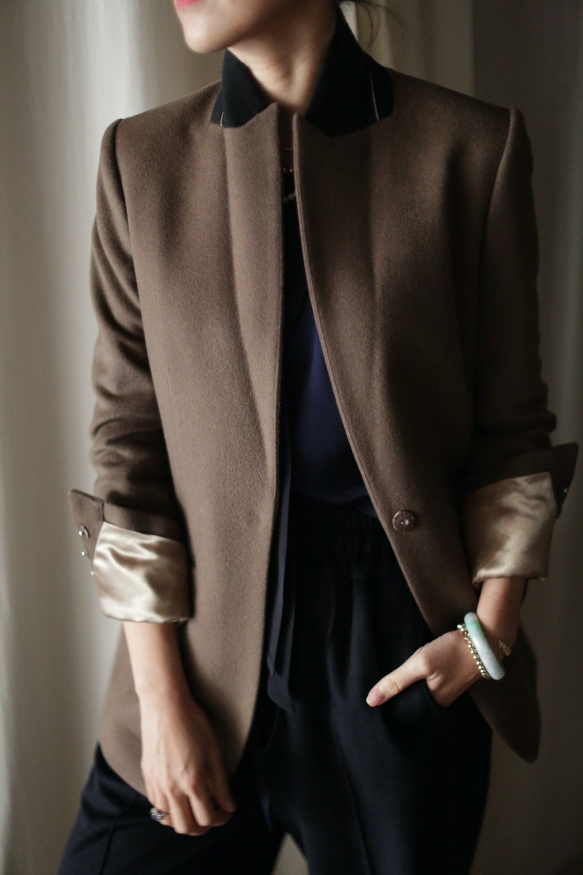 Sloane | Taupe / Black tuxedo jacket with a black collar and turned-up sleeves worn over a dark top and black trousers.