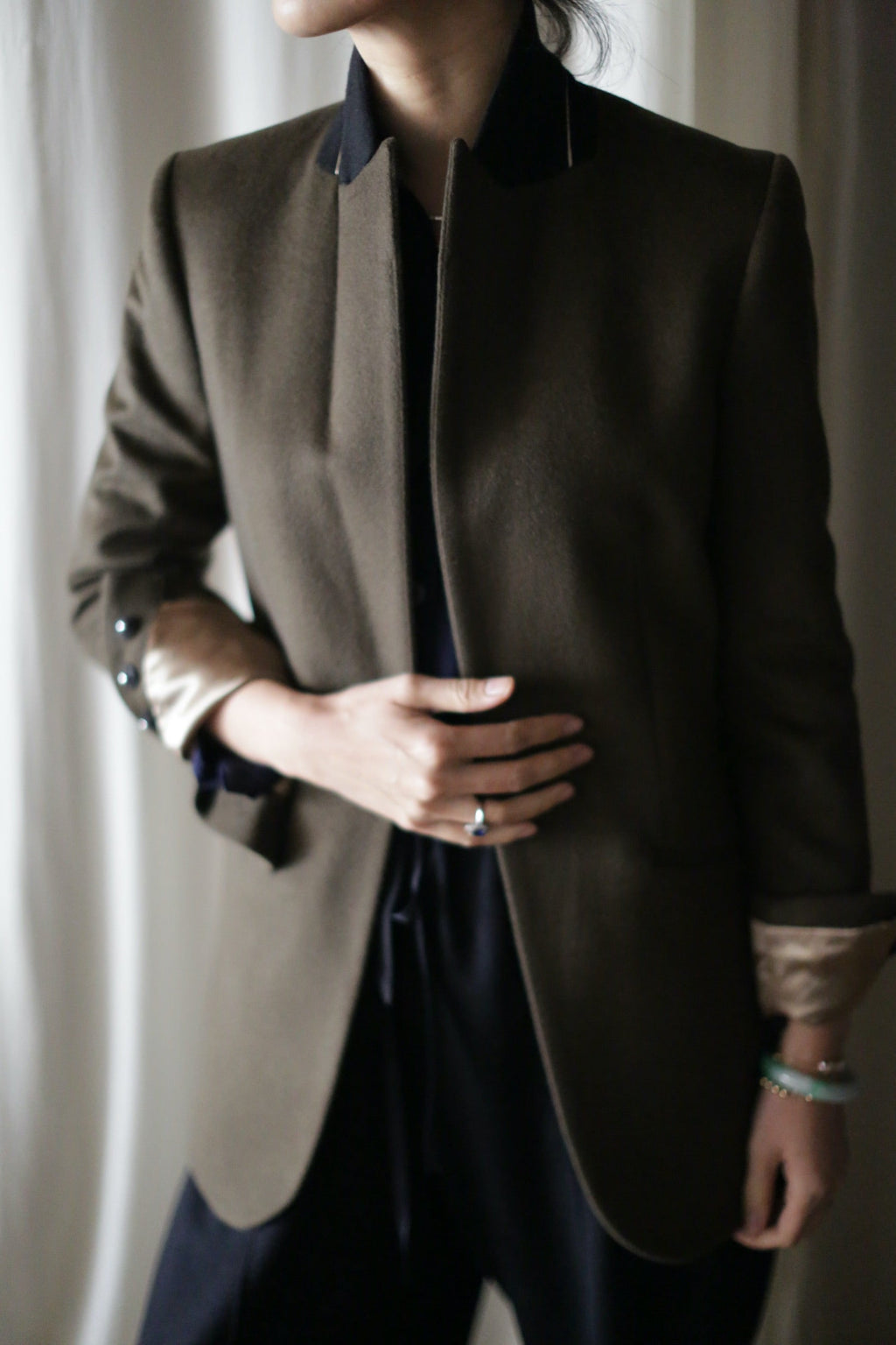 A person wearing a Sloane | Olive / Black woven cashmere tuxedo jacket with a black collar and turned-up cuffs over a black shirt.