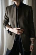 A person wearing a Sloane | Olive / Black woven cashmere tuxedo jacket with a black collar and turned-up cuffs over a black shirt.