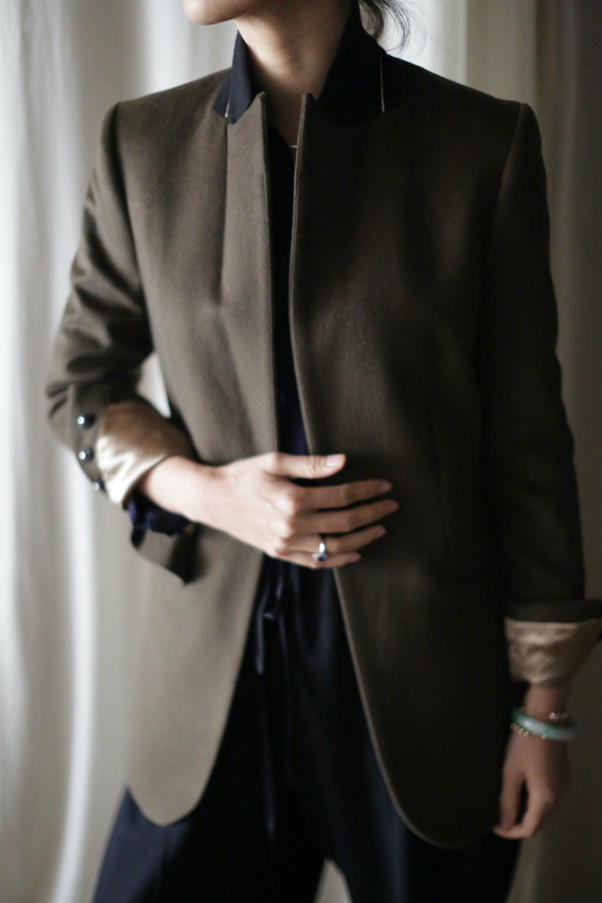 A person wearing an open, equestrian length Sloane | Taupe / Black tuxedo jacket over a black top.