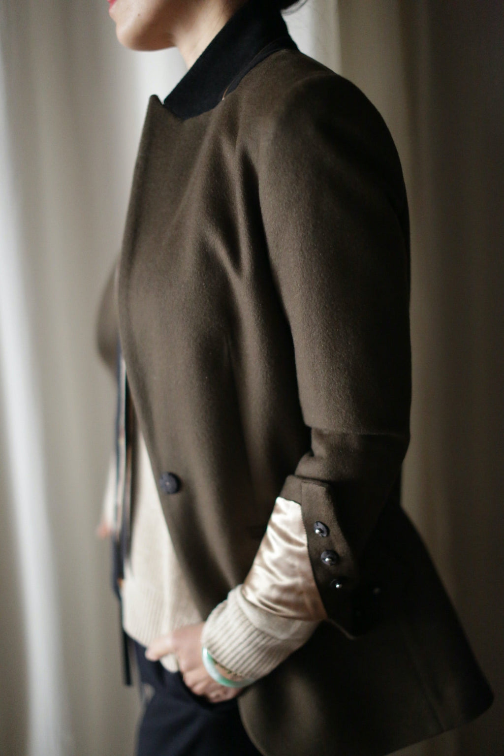 Sloane | Olive / Black equestrian-length coat with a black collar and buttons on the cuffs, worn over a cream-colored sweater.
