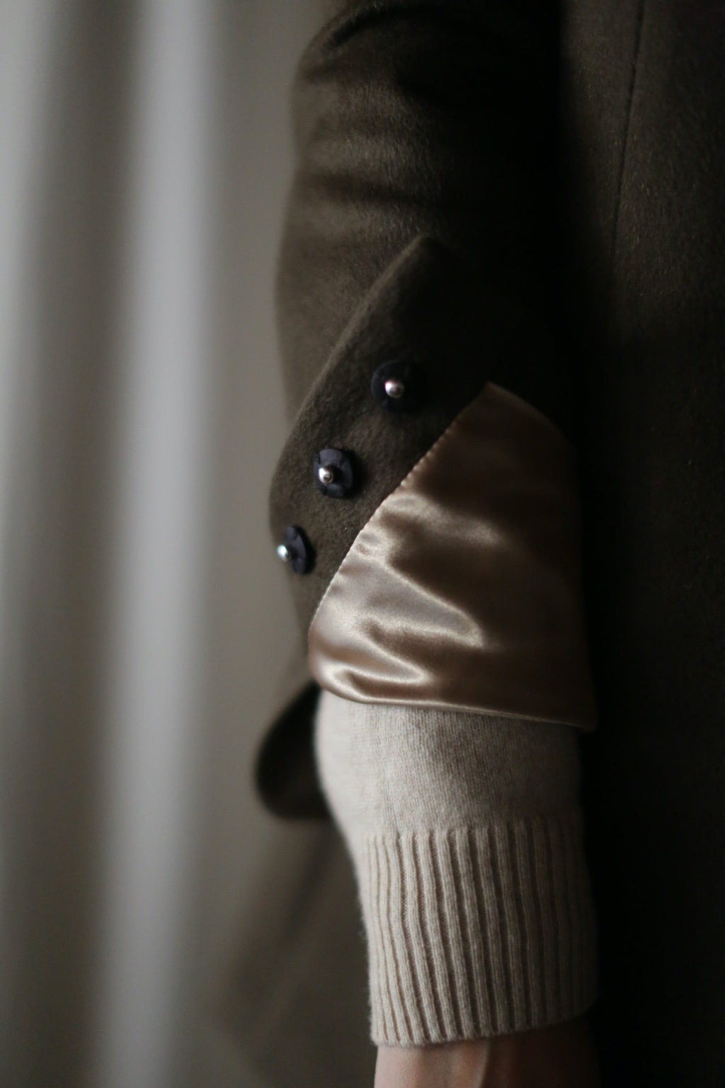 Sleeve of the Sloane | Taupe / Black cashmere coat featuring a folded cuff with three dark buttons and a beige knit underlayer.