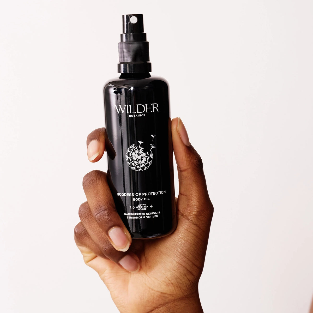 A hand holds the Goddess of Protection Body Oil in a black spray bottle. Infused with sandalwood, geranium, bergamot, vetiver, and enriched by grapeseed oil, it is set against a clean white background.