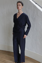 Load image into Gallery viewer, A person with short hair wears the X Blouse in Wool Pinstripe Navy and wide-leg trousers, standing indoors against a white textured wall and wooden floor, looking confidently at the camera.